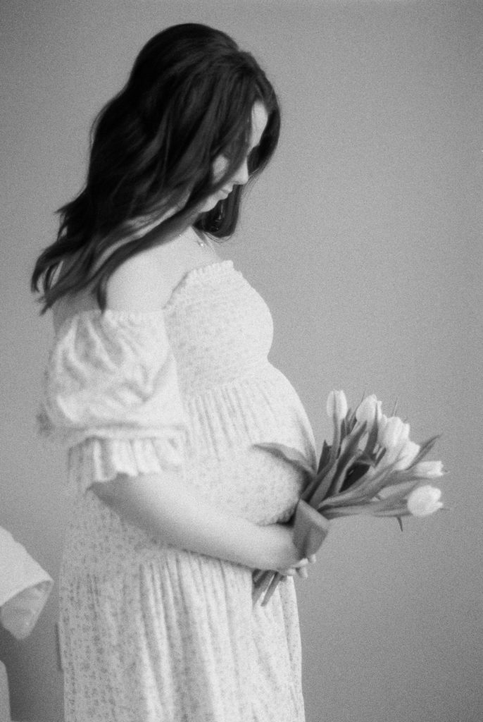 Expectant mother on black and white film, holding tulips against her growing bump captured by Edmonton maternity photographer, Kahla Kristen Photography