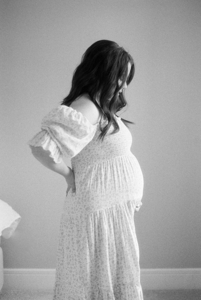 Beautiful expectant mother, cupping her bump in lovely floral dress on black and white film captured by Edmonton maternity photographer, Kahla Kristen Photography