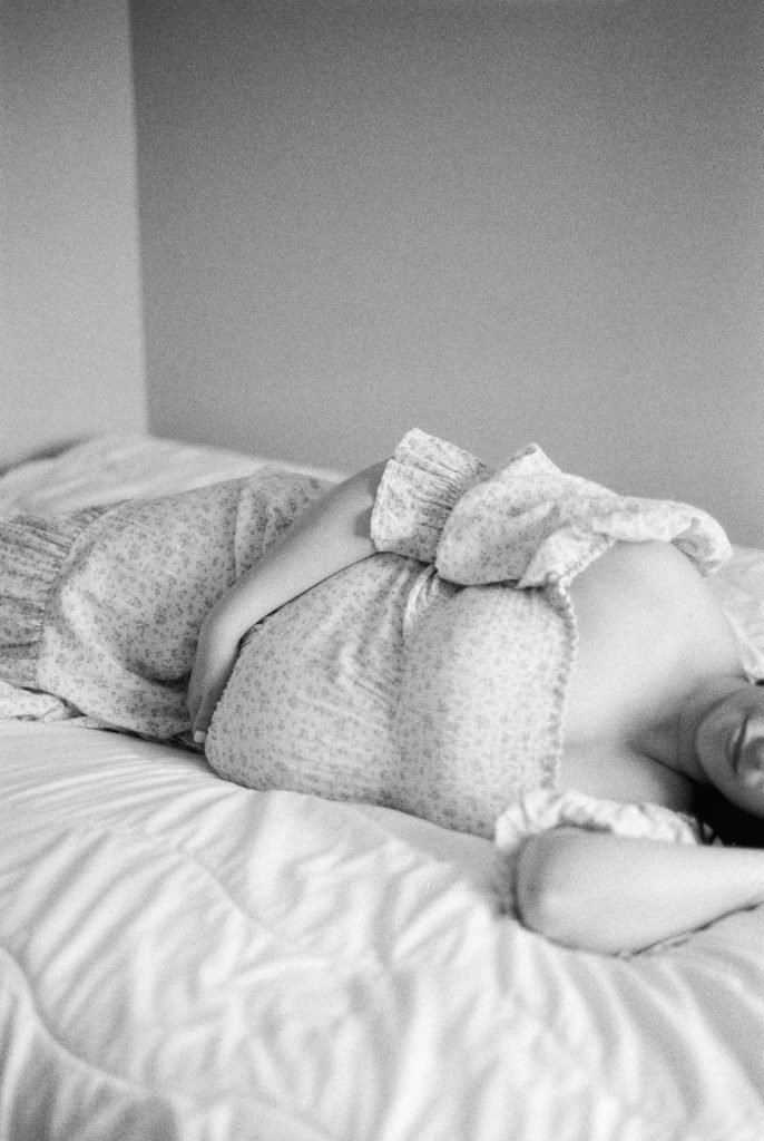 Expectant mother, snuggling her bump on the bed in a beautiful floral dress, shot on black and white film captured by Edmonton maternity photographer, Kahla Kristen Photography