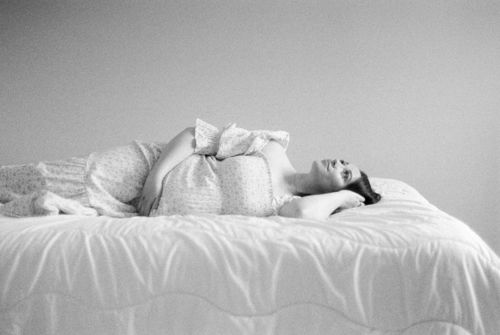 expectant mother in beautiful floral dress, laying on her back, captured on black and white film captured by Edmonton maternity photographer, Kahla Kristen Photography