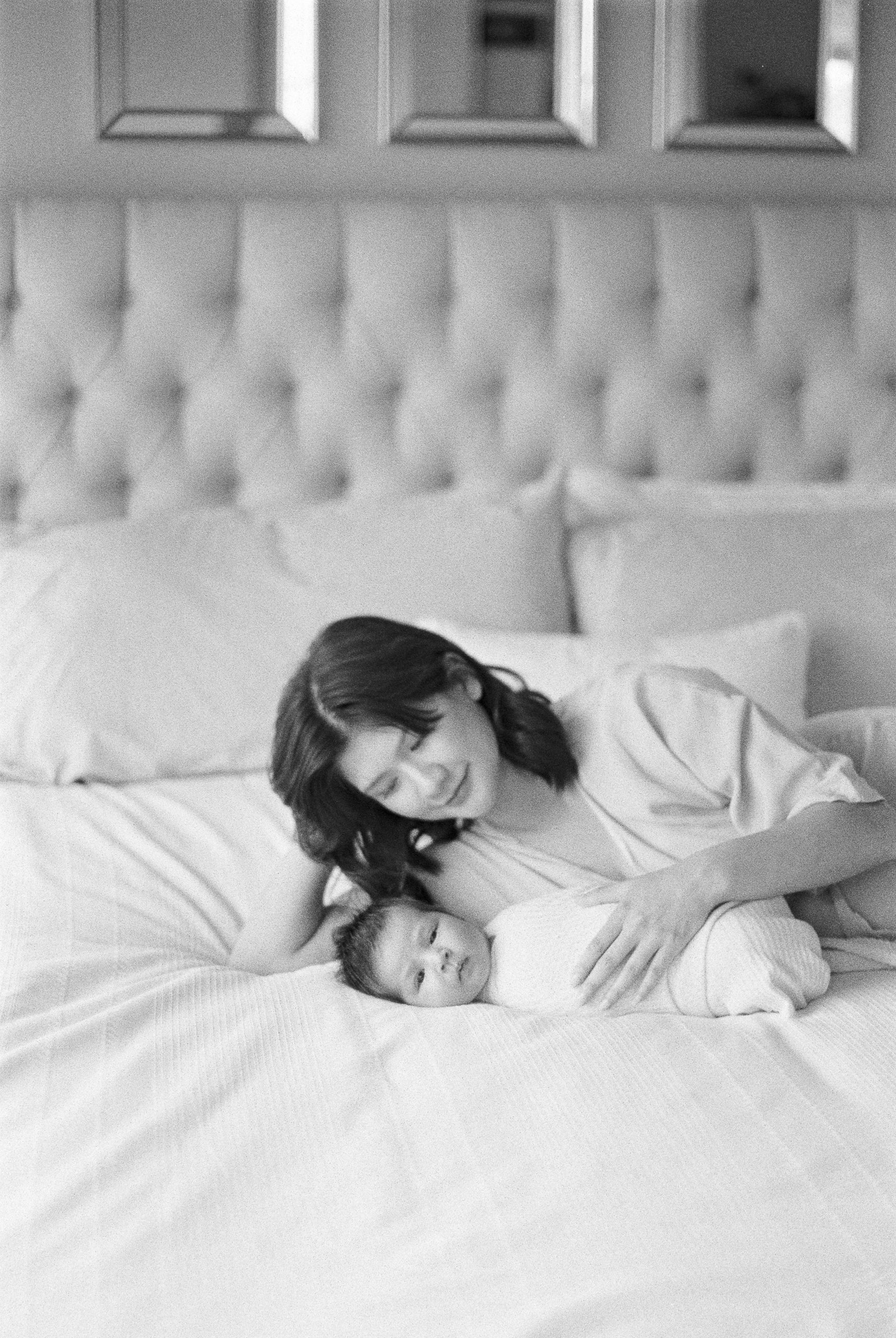 Mother snugging newborn baby on bed in black and white film