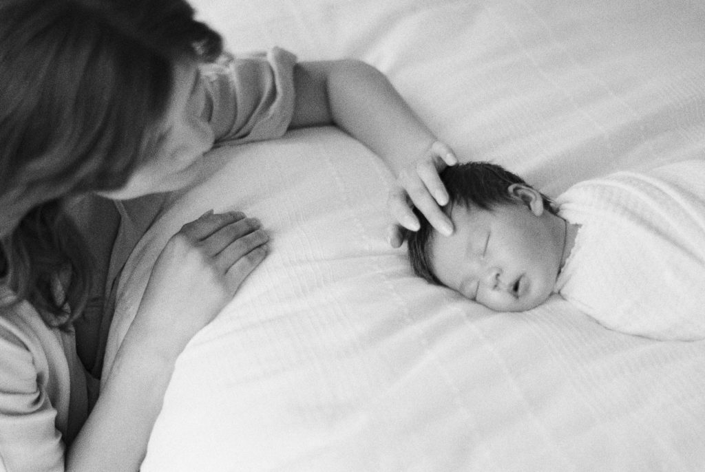 Mother gently calming sleeping newborn baby on black and white film