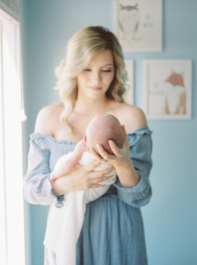 Mom cradling baby's head in her hand, smiling down at baby in newborn nursery