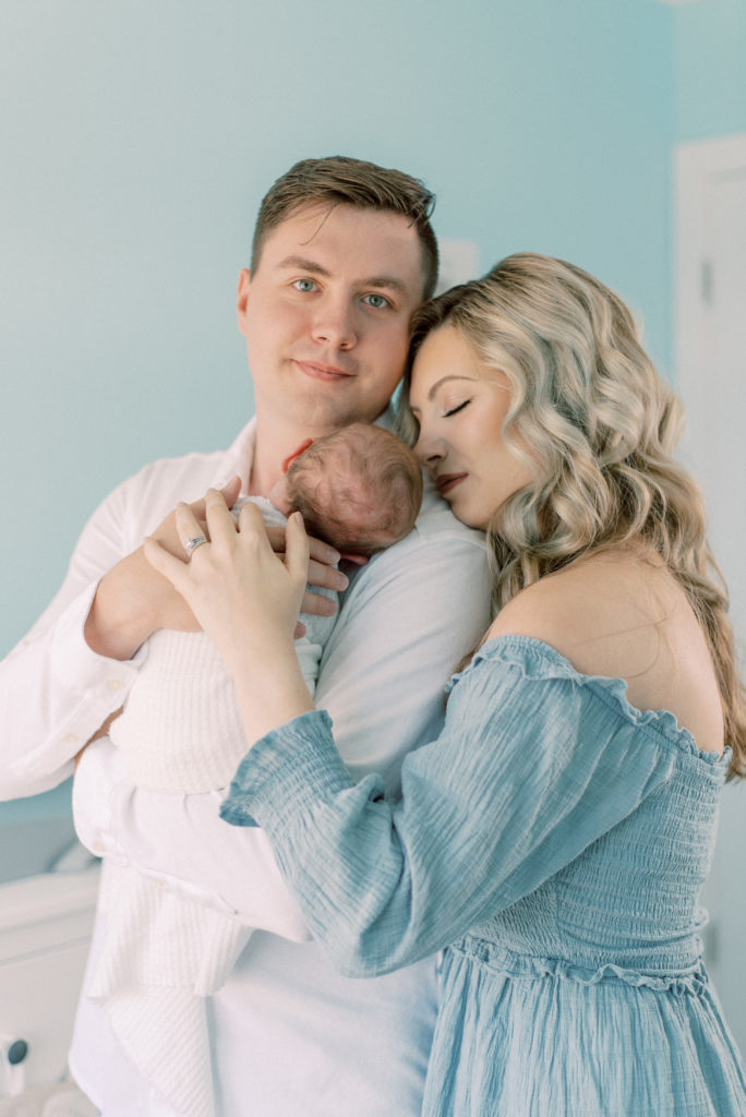 Dad holding baby and mom snuggling close in newborn baby nursery