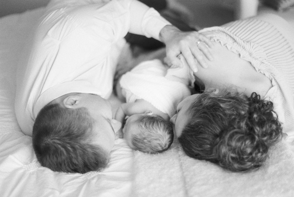 Edmonton Newborn Photography black and white image of dad, mom and baby snuggling, laying down on bed