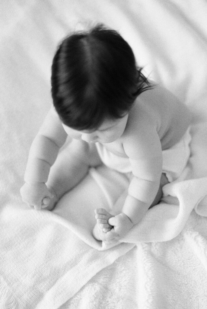 Six month milestone session near me. Baby sitting up grabbing toes. Captured on black and white film