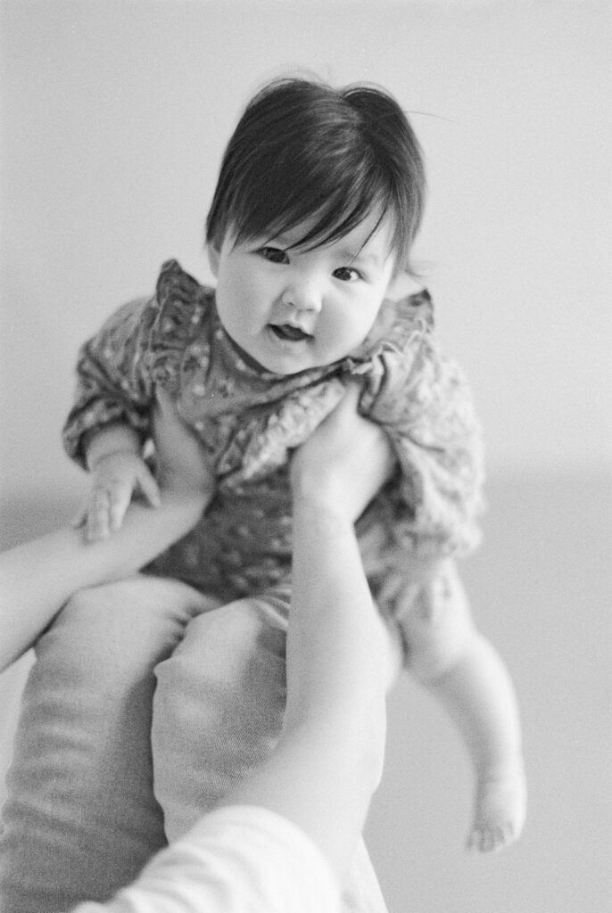 Six month milestone session near me. Baby flying on mom's legs. Captured on black and white film