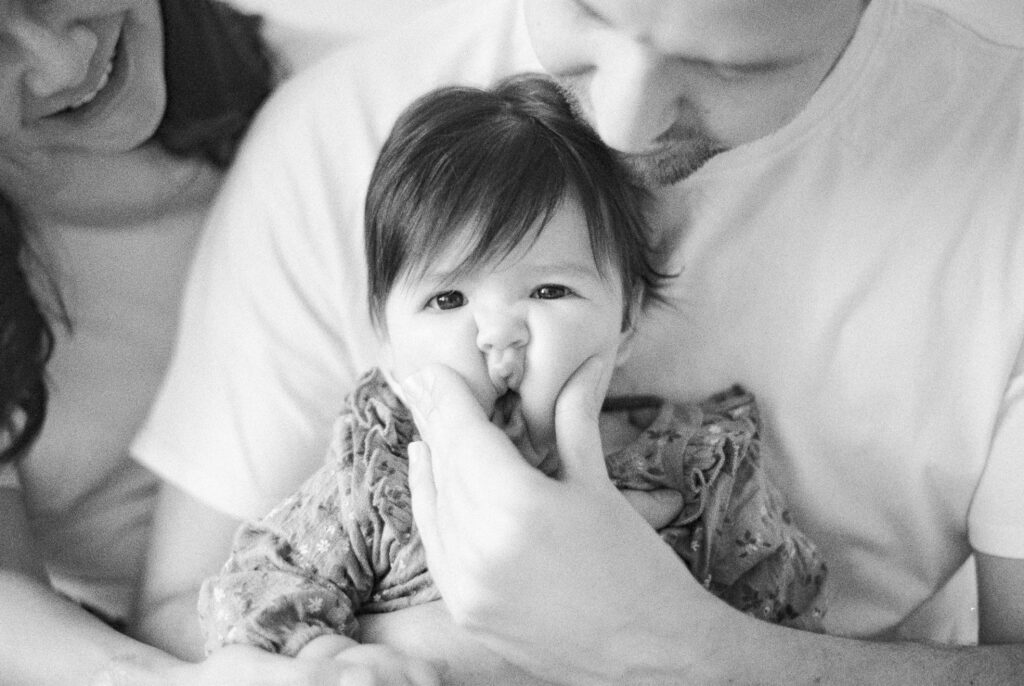 Six month milestone session near me. Baby's cheeks being squished by dad. Captured on black and white film