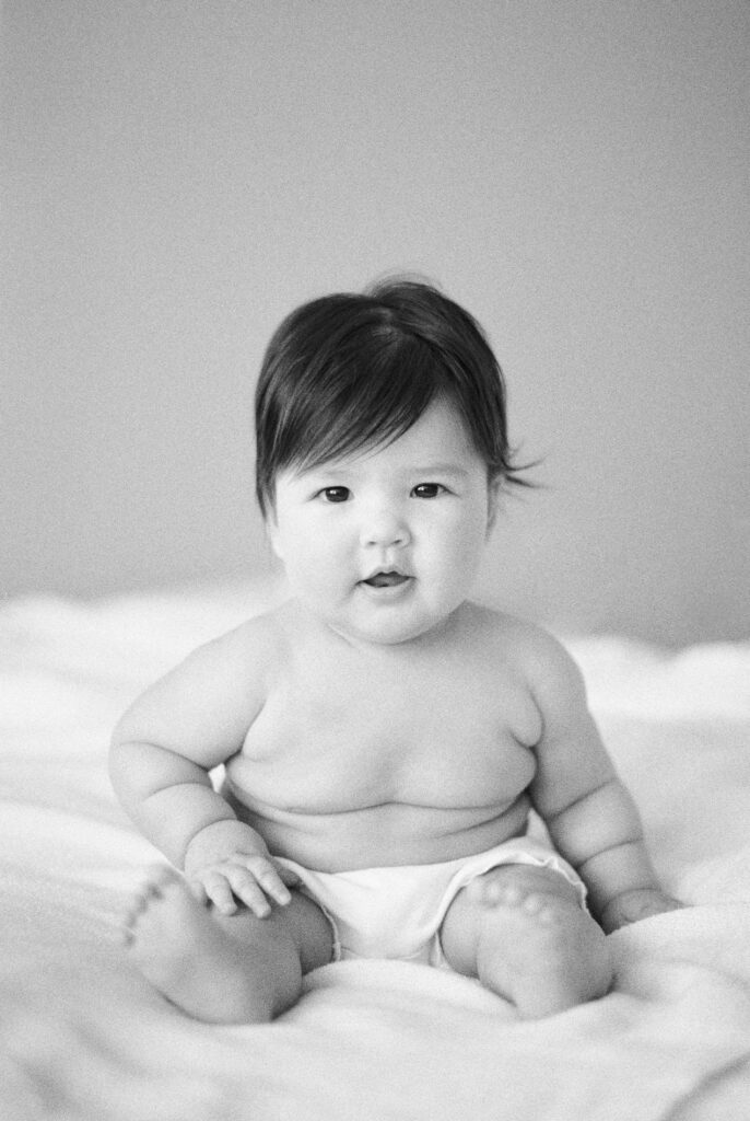 Milestone photography near me, photo of six month old baby girl sitting up on bed, captured on black and white film