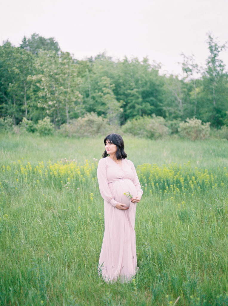 Expectant mother, standing in a pink dress in a field of wildflowers