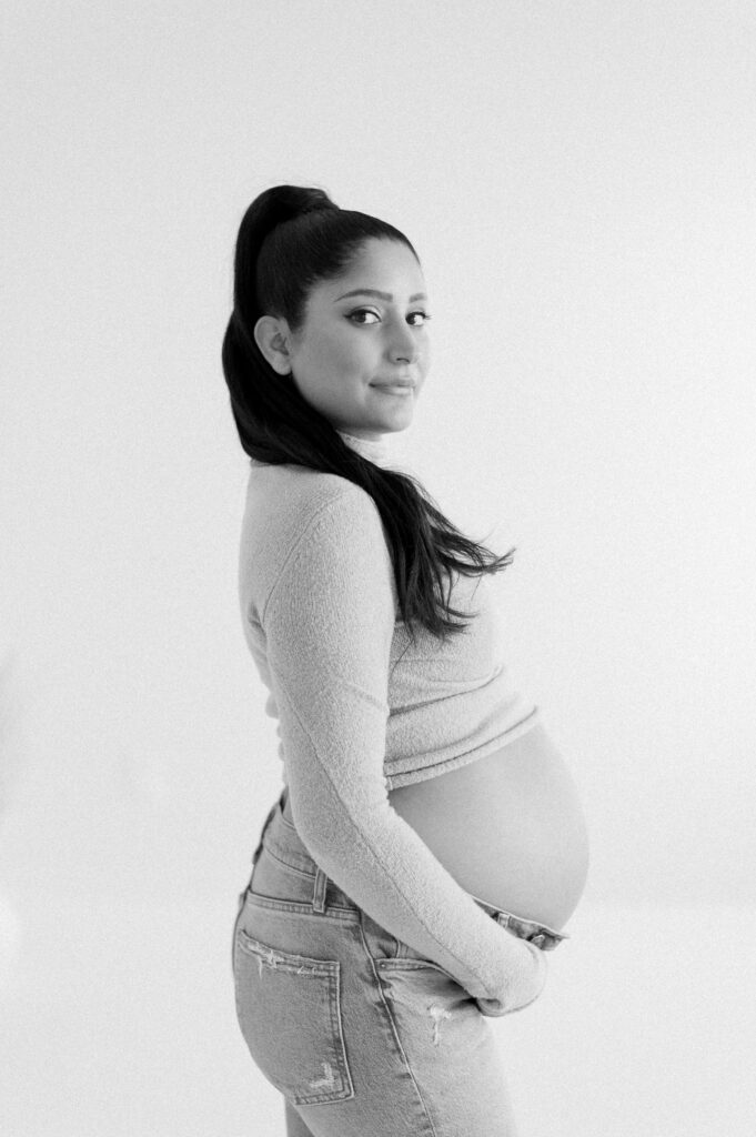 Edmonton photographer for beautiful maternity photos captures expectant mom in black and white smiling at the camera and cradling bump