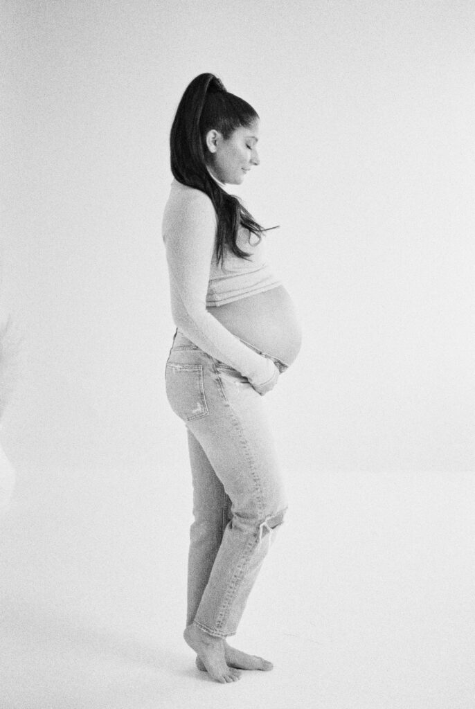 Expectant mother cradles bump, captured in studio on black and white film