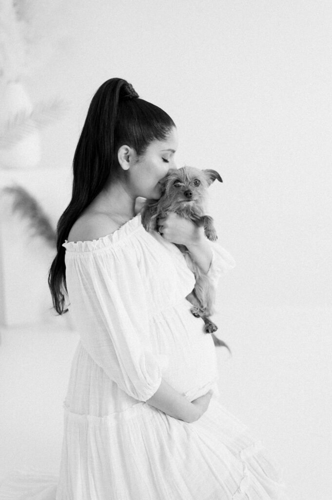 Expectant mom snuggles puppy in beautiful dress in studio