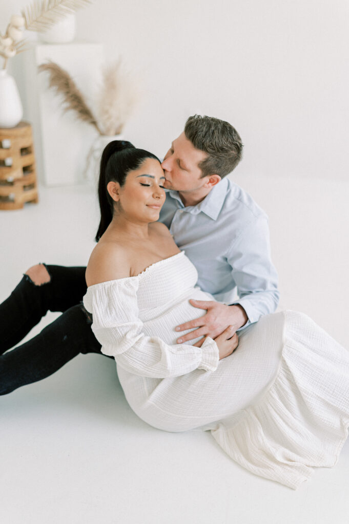 Mom and dad expecting baby, snuggling together on the floor in an all white studio