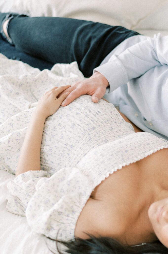 Expectant mom and dad snuggling together on a bed, cupping baby bump