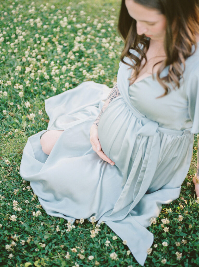 Mom laying in field of flowers, holding bump, sharing top 10 baby items for new moms