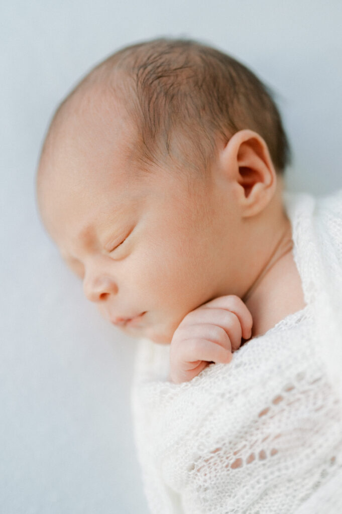 Infant wrapped in soft fabric with hand sticking out.