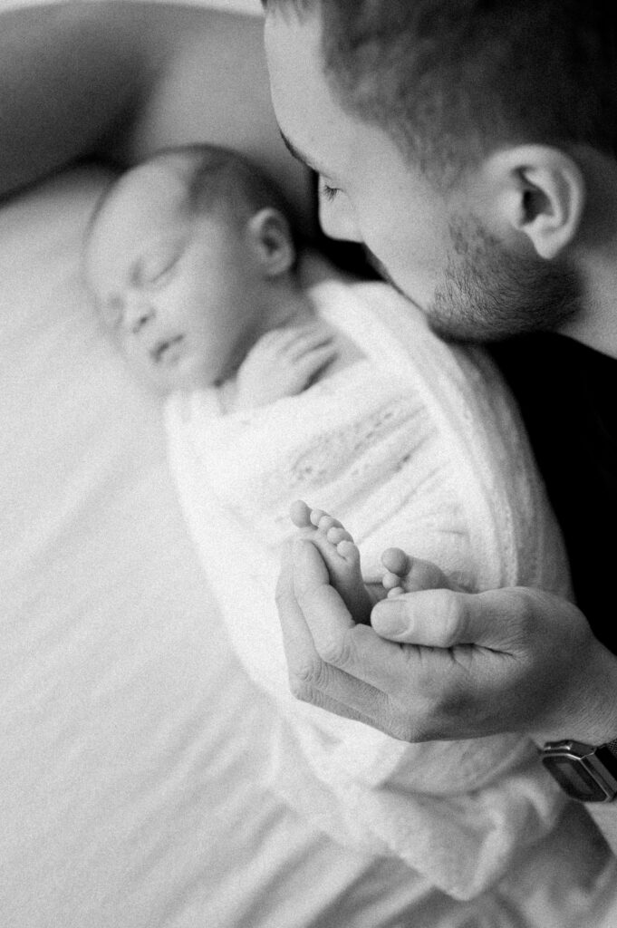 Parent holding baby's tiny feet while baby sleeps soundly on bed.